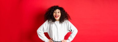 Heyecanlı pozitif kadın gülüyor ve gülümsüyor, neşeli hissediyor, kırmızı arka planda duran komik tanıtıma bakıyor..