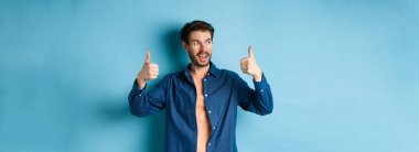 Yakışıklı genç adam boş alana bakıyor ve mavi arka planda dikiliyor..