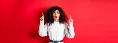 Günlük kıyafetlerle etkileyici Avrupalı kadın modeller, düşük çeneli tanıtımlara bakıyorlar, işaret ediyorlar, logoyu gösteriyorlar, kırmızı arka planda duruyorlar..