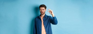 Kafkasyalı genç bir adamın görüntüsü, küçük boyda ve şaşı, mavi arka planda duran küçük bir şey görüyor..