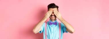 Gülümseyen yakışıklı adam görüntüsü. Gözleri kapalı, pembe arka planda şık kıyafetlerle bekleyen sürpriz bekliyor..