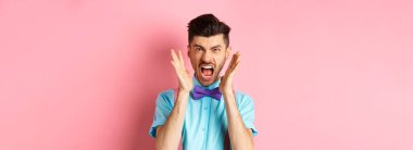 Kızgın adam deli gibi bağırıyor, el sıkışıyor ve kameraya öfkeli bakıyor, pembe arka planda kızgın duruyor..