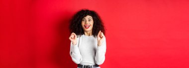 Heyecanlı kadın ödülü kazanıyor, seviniyor ve mutlu görünüyor, şaşkın bir şekilde gülümsüyor, kırmızı arka planda duruyor..