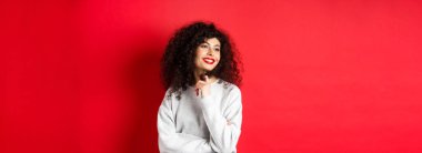 Kıvırcık saçlı, kırmızı dudaklı güzel bir kadın kıvırcık saçlı ve yana bakan, romantik bakışlı, stüdyo arka planında duran.