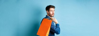 Arkaya bakan mutlu adam arkasını kolluyor ve mavi arka planda duruyor..