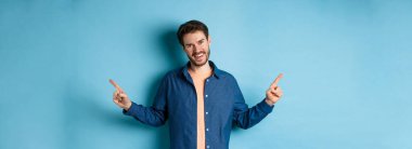 Sakallı, beyaz dişleriyle gülümseyen, iki seçeneği gösteren, mavi arka planda duran, beyaz saçlı yakışıklı beyaz adam..