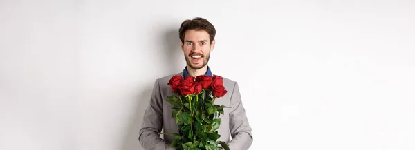stock image Excited handsome man in suit holding bouquet of roses for romantic date with lover, standing happy on Valentines day, white background.