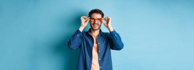 Mutlu beyaz adam yeni gözlük deniyor ve gülümsüyor, mavi arka planda duruyor..