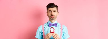 Sevgililer Günü. Üzgün erkek arkadaşının reddedilmesi, nişan yüzüğünü göstermesi ve somurtması, pembe arka planda durarak hayır dedi..