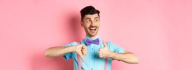 Neşeli adam soldan mutlu görünüyor, baş parmağını kaldırıyor, ürünü yargılıyor, olumlu ve olumsuz geri bildirim yapıyor, pembe arka planda duruyor..