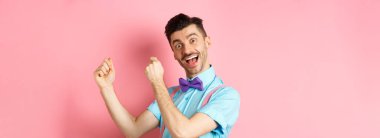 Neşeli bir adamın tatilini kutlaması, dans etmesi, eğlenmesi, zafer kazanması ve mutlu yüzüyle evet demesi, pembe arka planda durması..