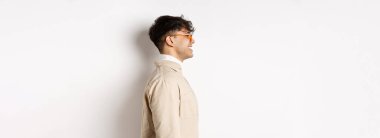 Gözlüklü yakışıklı beyaz adamın profili, boş yere bakıyor neşeli bir gülümsemeyle, beyaz arka planda duruyor..