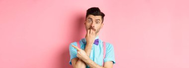 Papyonlu, cezbedici tırnaklarını yiyen, istediği bir şeyi işaret eden, pembe arka planda duran ilginç bir adam..