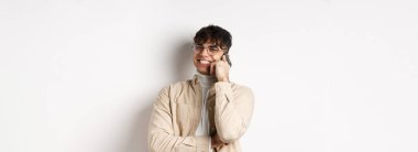 Gerçek insanlar konsepti. Cep telefonuyla konuşan mutlu genç adam, yana bak ve akıllı telefonu kulağına yakın tut, beyaz arka planda dur..