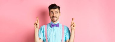 Umut dolu papyonlu yakışıklı adam, şans diliyor, şans diliyor ve sola bakıyor, sonuçları bekliyor ya da dua ediyor, pembe arka planda duruyor..