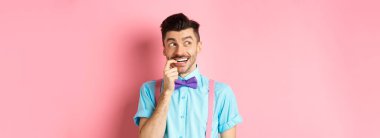 Gülümseyen bir adamın seçim yapması, hayalperest ve mutlu görünmesi, baştan çıkarıcı bir ifadeyle tırnağını yemesi, bir şey istemesi, pembe arka planda durması..