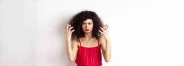 Öfkeli, kıvırcık saçlı, kırmızı elbiseli, öfkeden köpüren, kaşlarını çatan, öfkeli, beyaz arka planda duran öfkeli İtalyan kadın..