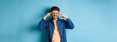 Hasta hisseden, başıyla temas eden, baş ağrısı çeken, baş dönmesi hisseden, mavi arka planda duran bir adam..