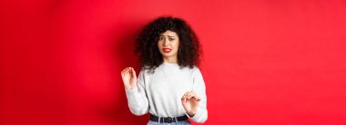 Tiksinmiş ve isteksiz bir kadın hayır diyor, ellerini kaldırıyor ya da reddediyor, durmak istiyor, rahatsız görünüyor, kırmızı arka planda duruyor..