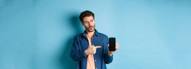 Uygulamadan bahseden yakışıklı bir adamın görüntüsü, hareket eden ekranı işaret eden ve mavi arka planda duran.