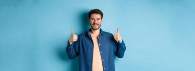 Yakışıklı, güler yüzlü, destekleyici, onay veren, iyi iş çıkaran, mavi arka planda mutlu duran..