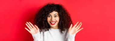 Şaşırmış ve mutlu kadının yakın çekimi harika haberler duyuyor, muhteşem bir olaya tepki veriyor, ellerini kaldırıyor ve sevinçten çığlık atıyor, eğleniyor, kırmızı arka planda duruyor..