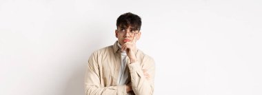 Üzgün ve yalnız genç adam üzgün yüzüyle boş alana bakıyor, beyaz arka planda düşünceli duruyor..