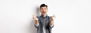 Heyecanlı romantik adam elini kaldırıyor ve kameraya gülümsüyor, sevgisini ve sevgisini ifade ediyor, beyaz arka planda duruyor..