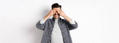 Mutlu, gülümseyen, gözleri kapalı bekleyen sürpriz bekleyen beyaz arka planda heyecanlı duran adam..