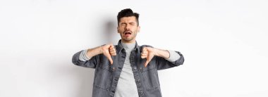 Üzgün adam ağlıyor ve baş parmağını aşağı gösteriyor, mızmızlanıyor ve şikayet ediyor, üzgün ve hayal kırıklığına uğruyor, beyaz arka planda duruyor..