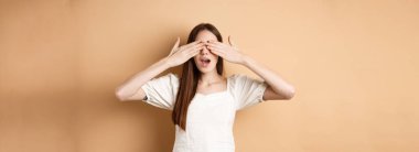 Mutlu romantik kız gözlerini kapatıyor ve sürpriz bekliyor, hediyeyi beklerken gülümsüyor, bej arka planda duruyor..