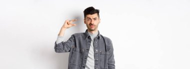 Hayal kırıklığına uğramış, küçük boylarda, suratını buruşturan üzgün, küçük şeylerden rahatsız olan, beyaz arka planda duran biri..