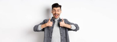 Kulağa hoş geliyor. Heyecanlı genç adam başparmağını kaldırıyor ve gülümsüyor mutlu, havalı bir şey öneriyor, iyi bir iş çıkarıyor, beyaz arka planda duruyor..