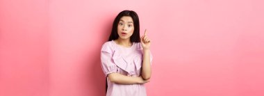 Heyecanlı Asyalı kadın bir fikir sunuyor, Eureka işaretinde parmağını kaldırıyor, planı ya da çözümü var, pembe arka planda duruyor..