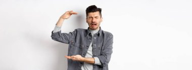 Üzgün adam ağlıyor ve büyük boy nesneler gösteriyor, büyük şeyleri şekillendiriyor ve şikayet ediyor, beyaz arka planda dururken hıçkırarak ağlıyor..