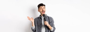 Heyecanlı stil sahibi adam konuşma yapıyor, mikrofonla konuşuyor, karaoke yapıyor ya da şarkı söylüyor, beyaz arka planda duruyor..