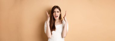 Meyveli kadın bağırıyor, el sıkışıyor, kızgın görünüyor, kızgın görünüyor, bej arka planda sıkıntılı duruyor..