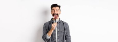 Yakışıklı, mükemmel dişleri ve dili olan, büyüteçle soldaki logoya bakan, beyaz arka planda duran bir adam..