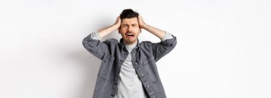 Hüsrana uğramış, ağlayan, panikleyen, ellerini başının üstüne koyup bağıran, sıkıntılı, beyaz arka planda üzgün duran bir adam..