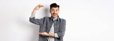 Neşeli adam gülümsüyor ve büyük boy gösteriyor, büyük bir şey gösteriyor ve heyecanlı görünüyor, beyaz arka planda duruyor..