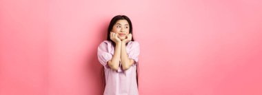 Hayalperest romantik kız logoya bakıyor ve gülümsüyor, güzel bir şey düşünüyor, pembe arka planda duruyor..