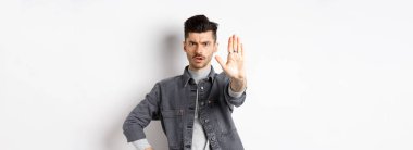 Ciddi bir adam durmasını, bir şeyi yasaklamasını ve kaşlarını çatmasını söyler, hayır der, elini beyaz arka plana uzatmaktan rahatsız olur..