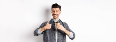 Çok iyi bir içki. Gülümseyen stil sahibi, kahve içen, başparmağını kaldıran, kahveciye övgüler yağdıran, beyaz arka planda duran.