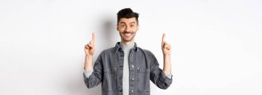 Heyecanlı genç adam gülümsüyor ve reklamını yapıyor, reklam teklifini işaret ediyor, beyaz arka planda duruyor..