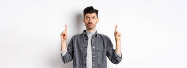 Üzgün, kaşları çatık adam yukarı bakıyor, beyaz arka planda tereddütlü duruyor..