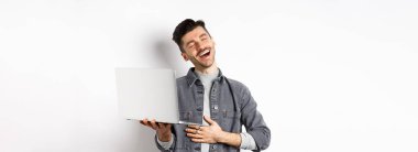 Dizüstü bilgisayardaki komik videolara gülen, göbeğine dokunan ve gülümseyen mutlu adamın görüntüsü..