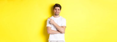 Şüpheci ve keyifsiz bir adam topal, isteksiz, sarı arka planda duran bir şeyi işaret ediyor..