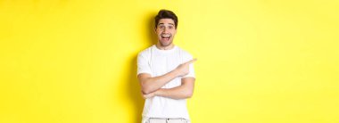 Mutlu adam solu işaret ediyor, fotokopi alanının reklamını yapıyor, gülümsüyor, beyaz elbiseler içinde sarı arka plana karşı duruyor..