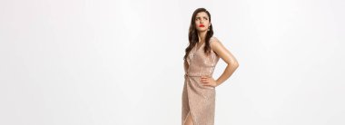 Noel partisi ve kutlama konsepti. Canı sıkkın, kaşlarını çatmış, yan yan yan bakan, şaşaalı bir elbise içinde beyaz arka planda duran kıskanç bir kadın..