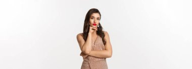 Kutlama ve parti konsepti. Cazibeli elbiseli güzel bir bayan model kameraya düşünceli bakıyor ve karar veriyor, beyaz arka planda duruyor..